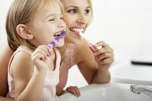 A mom and her daughter brushing their teeth happily