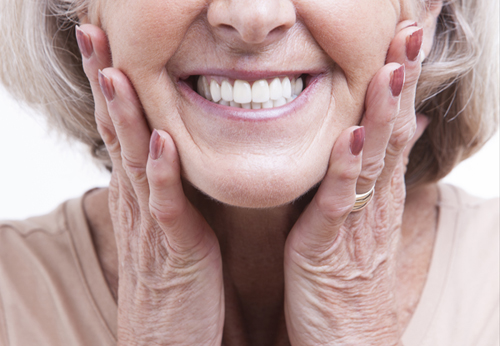 An old woman smiling with a complete set of teeth and her hands on her cheeks